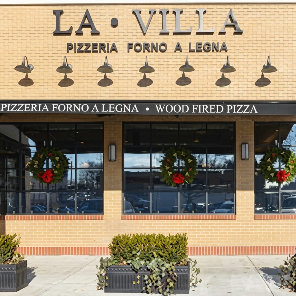 La Villa pizzeria storefront with brick facade, wood-fired pizza signage, wreath-decorated windows, and outdoor planters.