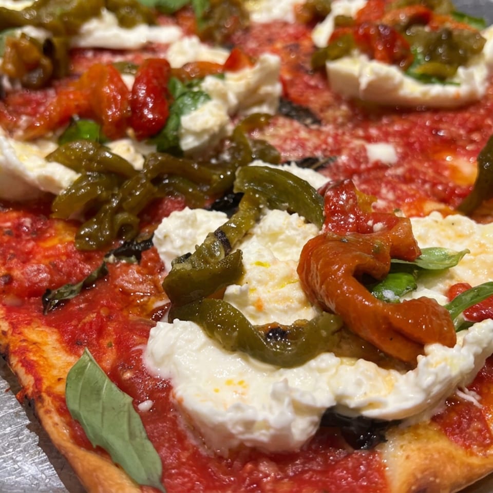 Rectangular pizza topped with tomato sauce, fresh burrata, roasted peppers, green chilies, and basil on a metal tray.